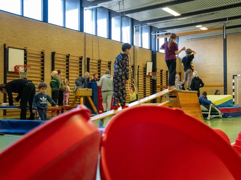 Mange redskaber er ude i en lille gymnastiksal og børnene løber rundt på balancebomme mm.