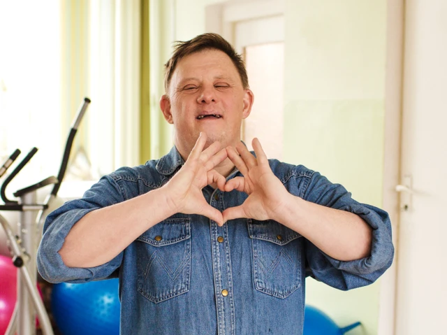 En mand med Downs Syndrom former med sine hænder et hjerte foran sit bryst. Han står i et træningslokale.