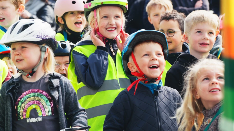 En flok af glade børn med cykelhjælpe kigger op mod en scene.