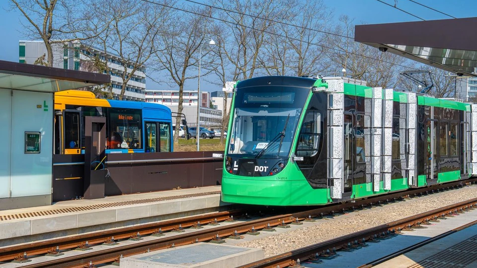 Et letbanetog på skinnerne ved en station og med en S-bus i baggrunden.