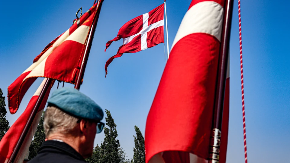 En mand med en blå barret står mellem to faner med kig til en flagstang med Dannebrog.