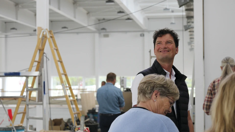 Mand kigger op og ud af billedet. Han står i en gruppe af folk, som kigger på en byggeplads.