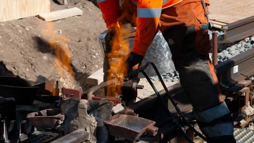 En arbejdsmand står med et apparat, der afgiver flammende varme. Han står henover nogle skinner.