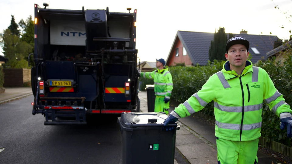 To skraldemænd ved en skraldebil, en trækker med spanden, en vipper mekanismen.