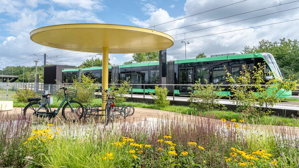 Letbanen holder på en station, i forgrunden cykelstativ og sommerblomster