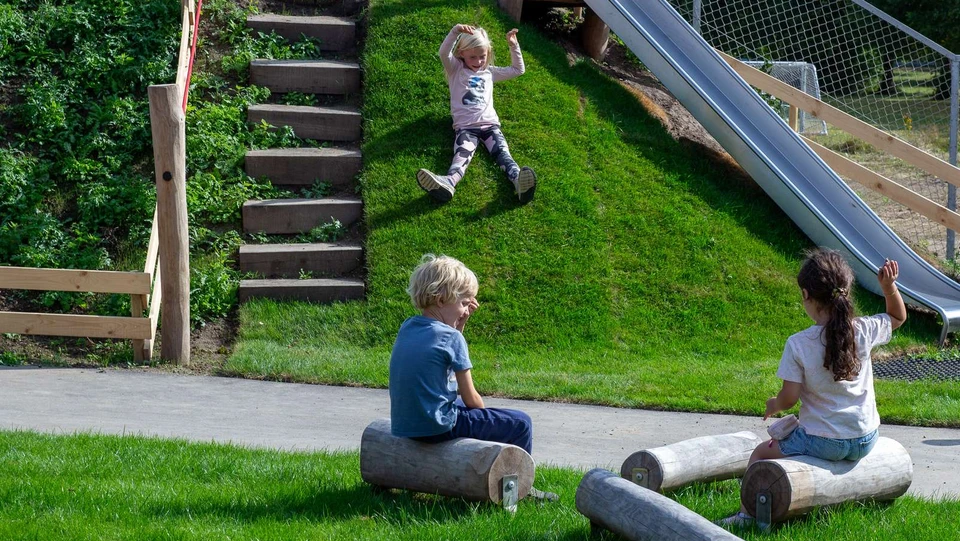 Pige rutsjer ned af grøn græsbakke ved siden af rutsjebane