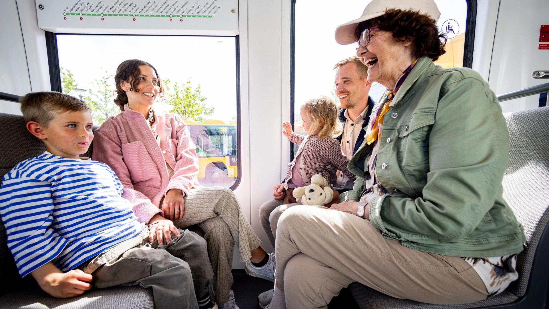 En familie med to børn og en bedstemor sidder i en kupé i den nye letbane og griner sammen