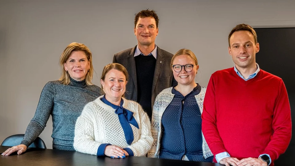 Fem personer står ved et bord og smiler til fotografen