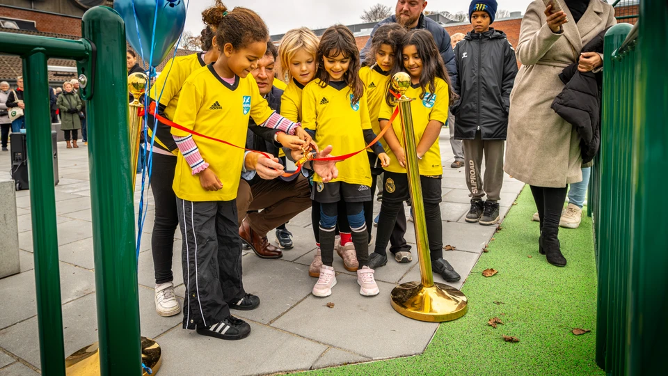 En masse piger i fodboldtrøjer hjælper borgmesteren med at klippe en rød snor