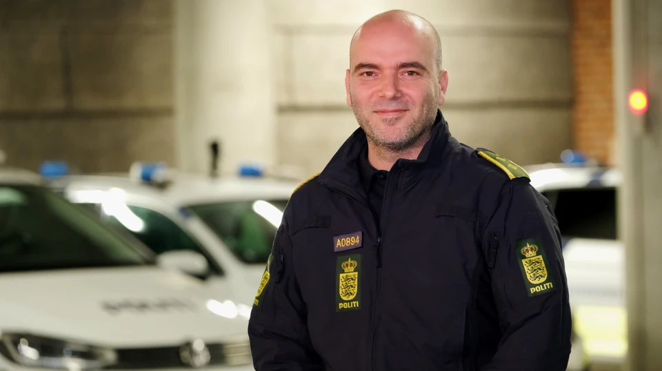 Uniformeret betjent står foran politibiler i en parkeringskælder