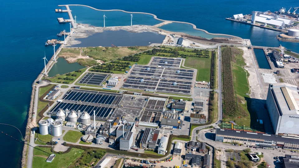 Luftbillede over område med siloer, bassiner, indsø og vindmøller.