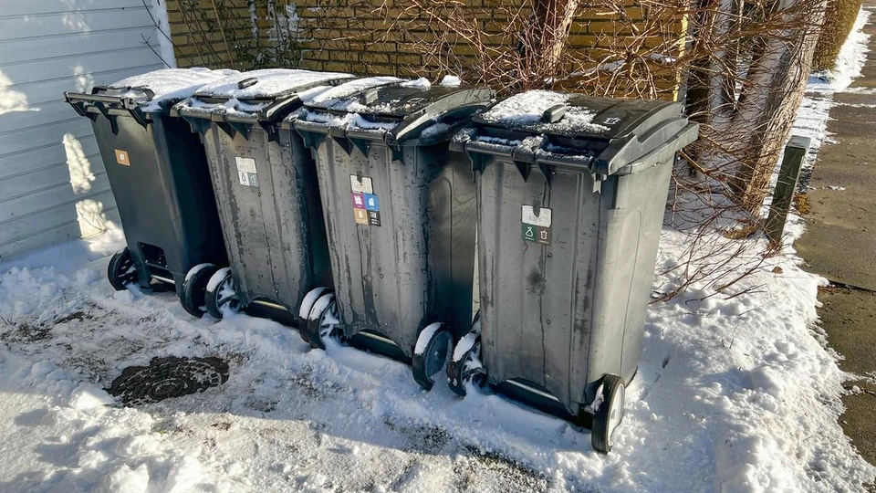 Fire affaldsspande, der står ved skel tæt på en gul murstensbolig.