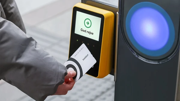 En hånd holder et plastikkort hen til en scanner, der på displayet ønsker "god rejse"