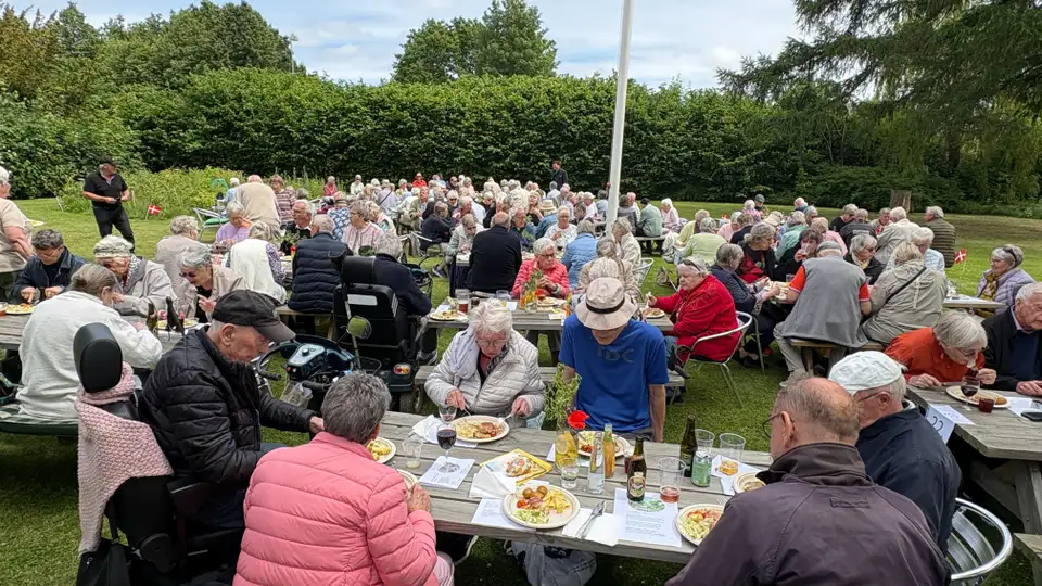 Sommerfestdeltagere ved borde i haven på Korsagergård