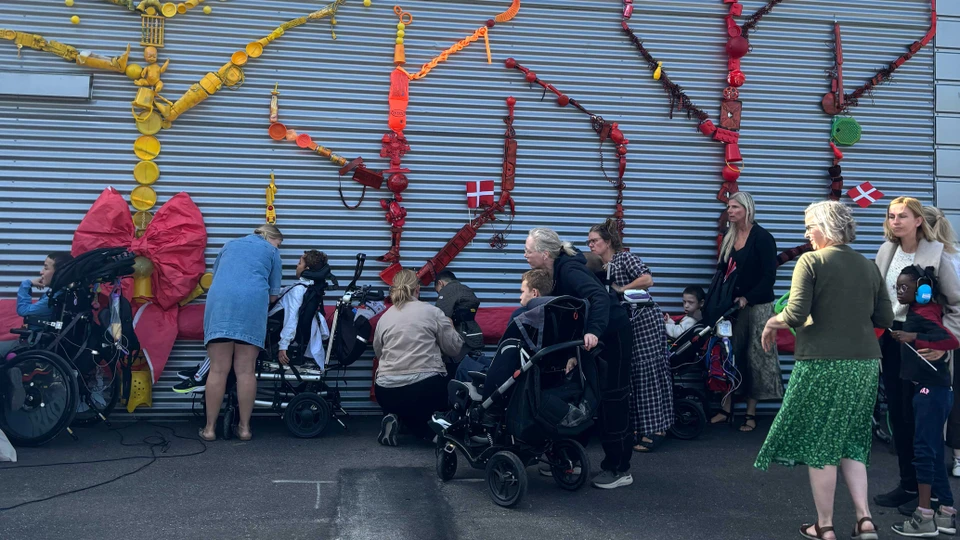 En masse multihandicappede børn og deres hjælpere river et gigantisk rødt bånd over for at afsløre kunstværket.