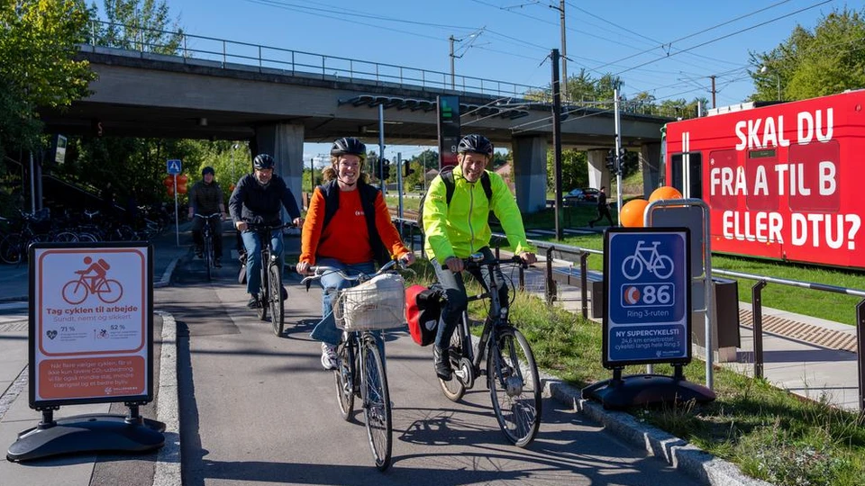 Et felt af cykelister der kører ved imellem en port af skilte om supercykelstien og balloner i baggrunden.